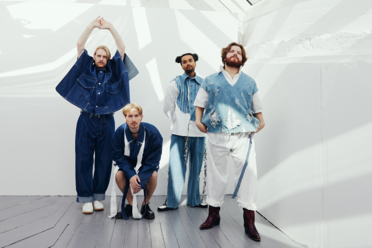 Bildet viser de fire bandmedlemmene i Tøfl stående foran en hvit vegg, dramatisk poserende i matchende dongeri-antrekk